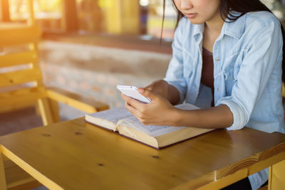 Midsection of woman reading book while sitting on table