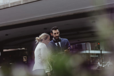 Entrepreneur and female coworker looking at smart phone while standing in city