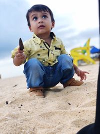 Thoughtful baby boy playing with sand at beach