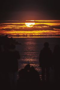 Silhouette people looking at sea during sunset