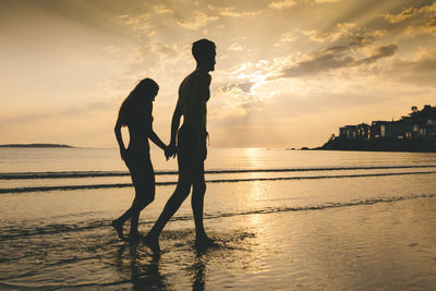 Silhouette couple on beach against sky during sunset