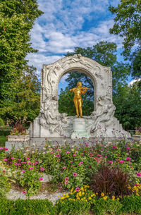 Statue amidst flowering plants against sky