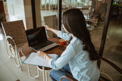 Rear view of woman using laptop at table