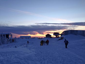 People on snowy landscape against sky during sunset