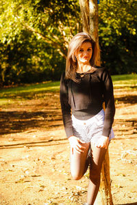 Portrait of beautiful woman standing against tree trunk at park