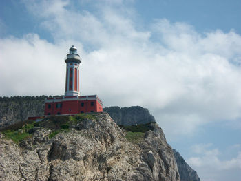 Lighthouse on cliff by sea against sky