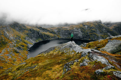 Hiking man at cliff edge with scenic view of lake and mountains at munkebu in lofoten norway