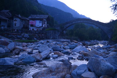 Rocks by river and buildings against sky