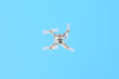 Low angle view of drone flying against clear blue sky