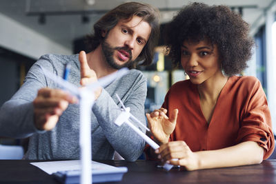 Business couple discussing over windmill model at table in office