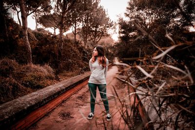 Full length portrait of young woman standing against trees