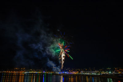 Firework display over city against sky at night