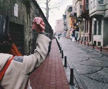 Cropped image of woman with hand raised standing on street amidst buildings