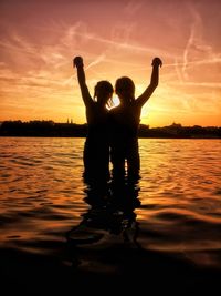 Silhouette woman with arms raised in sea during sunset