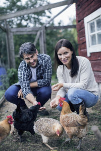 Portrait of happy couple feeding hens at poultry farm