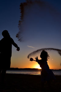 Silhouette people at beach against sky during sunset