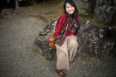 Full length portrait of smiling young woman sitting on rocks