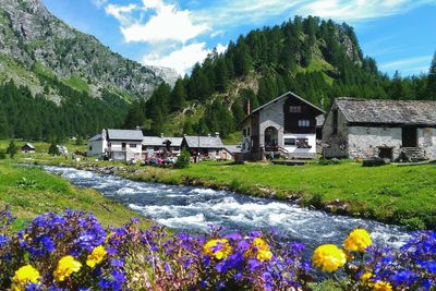 River flowing by houses against mountains on sunny day