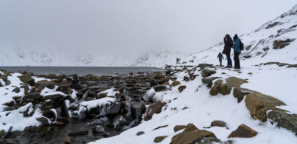 People walking on snow covered land against sky