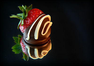 Chocolate covered strawberry with reflection against black background