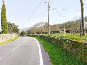 Empty road by trees against sky