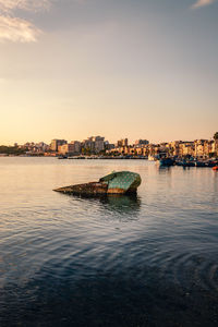 Boats in river by buildings in city against sky during sunset