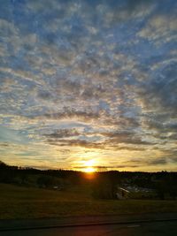 Silhouette of field against cloudy sky at sunset