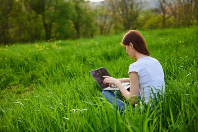 Young woman using mobile phone while sitting on grassy field