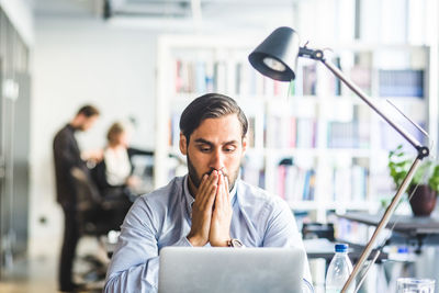 Tensed businessman covering mouth while looking at laptop in office