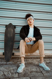 Full length of young man sitting on seat against wall