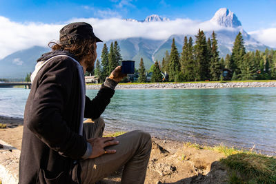 Man sitting by lake against sky