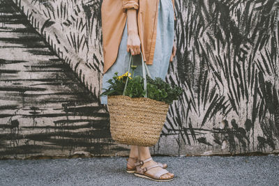 Woman with leafy vegetables and flowers in wicker bag by patterned wall