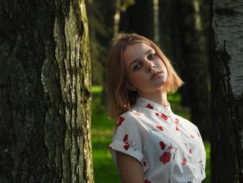 Portrait of young woman standing by tree trunk in forest