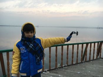 Boy standing by railing against sea during sunset