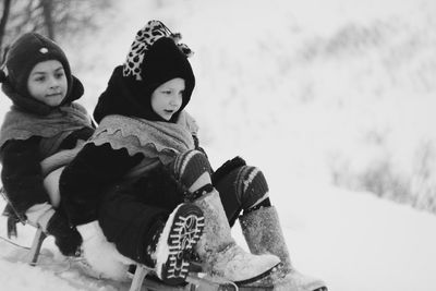 Brothers tobogganing on snow covered field in forest