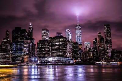 Illuminated buildings by river against sky at night