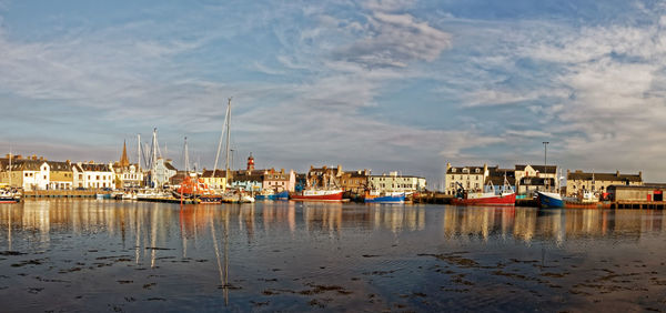 Sailboats in sea by buildings against sky