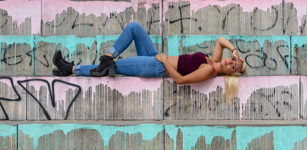 Full length side view of woman lying on graffiti wall