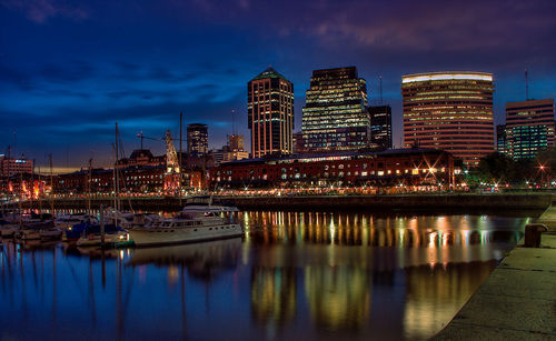 Boats moored at harbor with illuminated buildings in city against sky