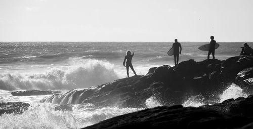 Surfers standing on rocks looking at big waves