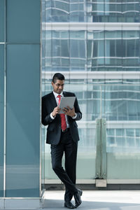 Businessman using digital tablet while standing against window in office