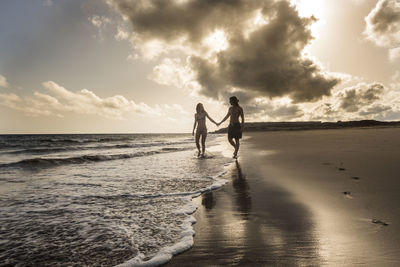 Man and woman holding hands at the beach during sunset