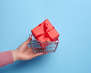 Cropped hand of woman holding gift against blue background