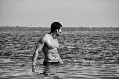 Rear view of shirtless boy playing in sea against clear sky