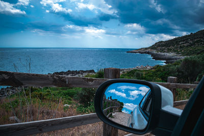 View of sea seen through side-view mirror