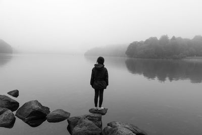 Rear view of man standing on rock by lake