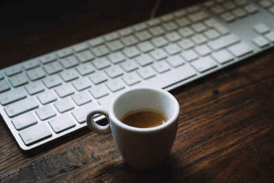 High angle view of coffee cup by keyboard on table