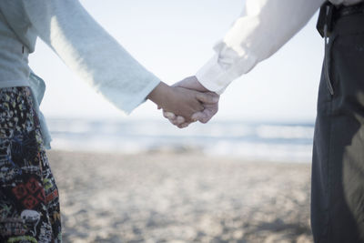 Midsection of couple holding hands at beach