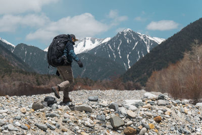 Side view of backpacker walking on land with mountains in background