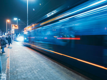 The tram leaves the stop in night city, motion blur view